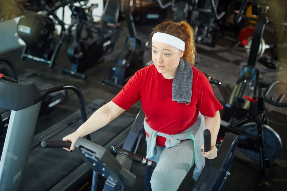 overweight woman with red hair training using elliptical machines in gym