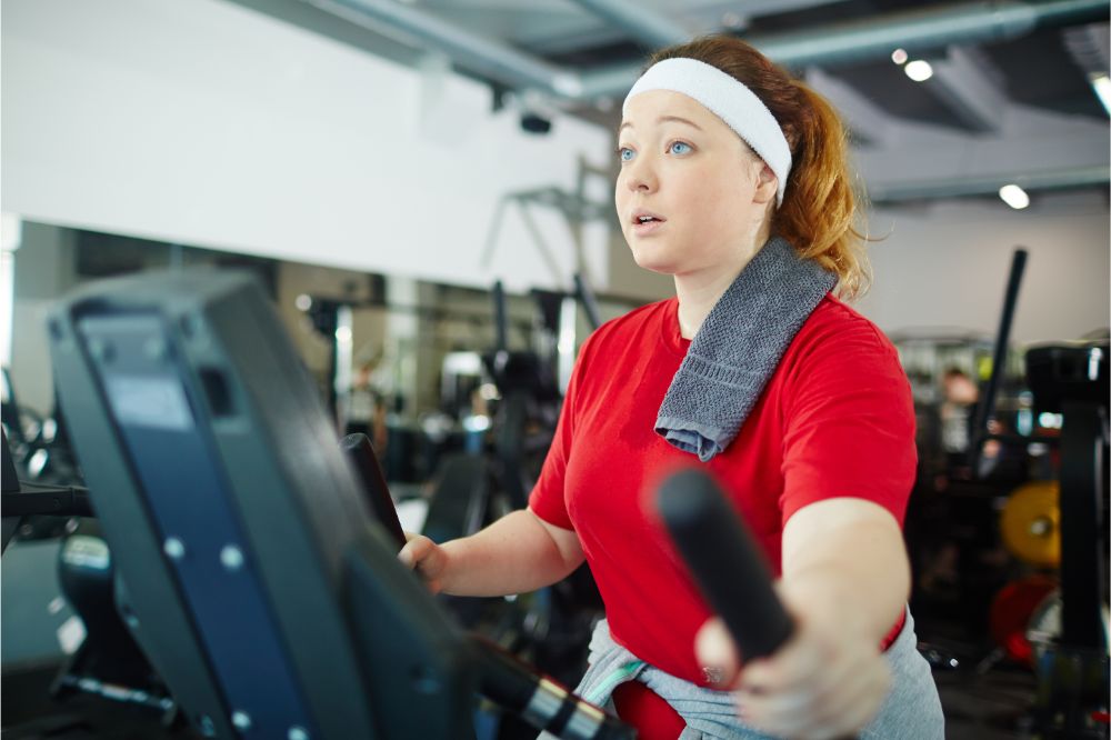 Portrait of cute overweight woman with red hair working out using machines 